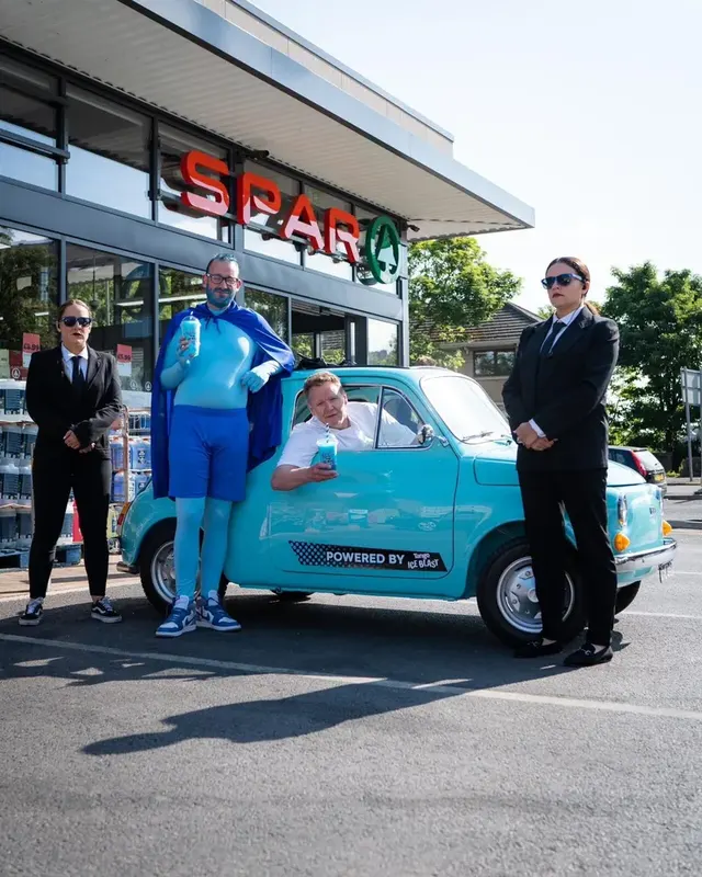 The blue Tango Ice Blast character and lookalikes beside a turquoise vintage car outside a Spar shop.