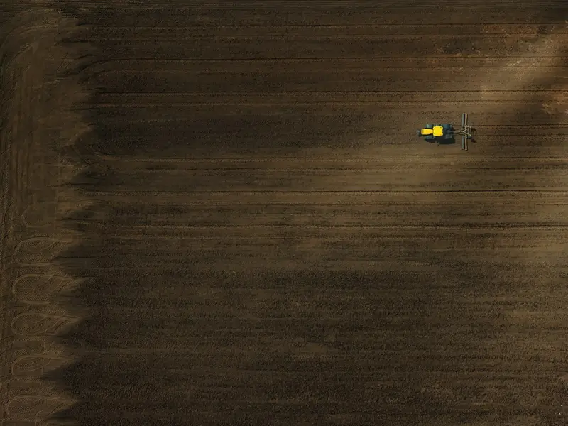 A yellow tractor working a dark ploughed field, seen from the air.